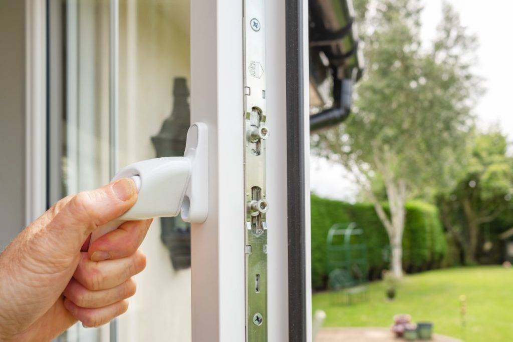 A close up of a mans hand opening a window to a back garden.
