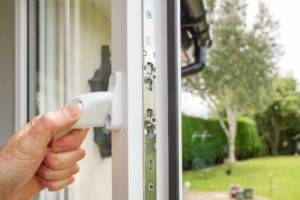 A close up of a mans hand opening a window to a back garden.