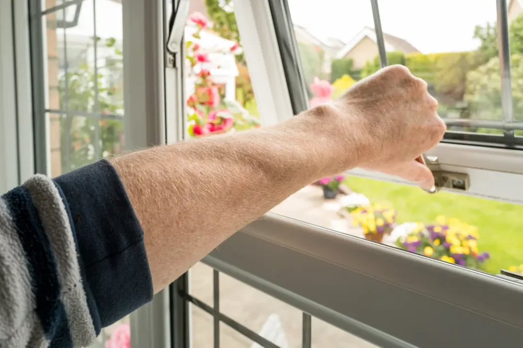 Homeowner seen about to lock a double glazed window seen on the ground level of a property. The latch can itself be locked to enhance security.